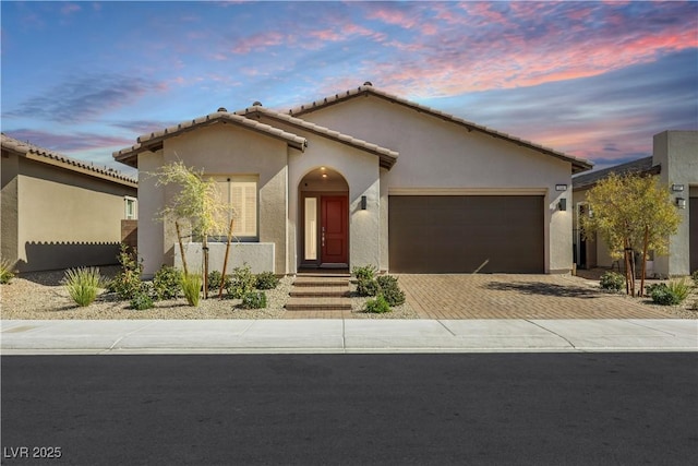 view of front of home with decorative driveway, an attached garage, a tile roof, and stucco siding