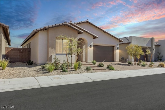 view of front of house featuring a garage, fence, driveway, a tiled roof, and stucco siding