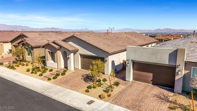 view of front of property with an attached garage, a mountain view, a tile roof, decorative driveway, and stucco siding