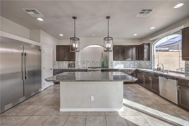 kitchen with dark brown cabinets, appliances with stainless steel finishes, a kitchen island, and visible vents