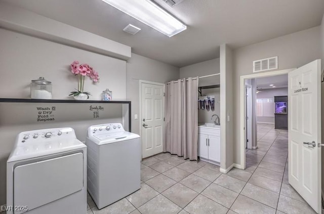 washroom with a sink, light tile patterned floors, washing machine and clothes dryer, and visible vents