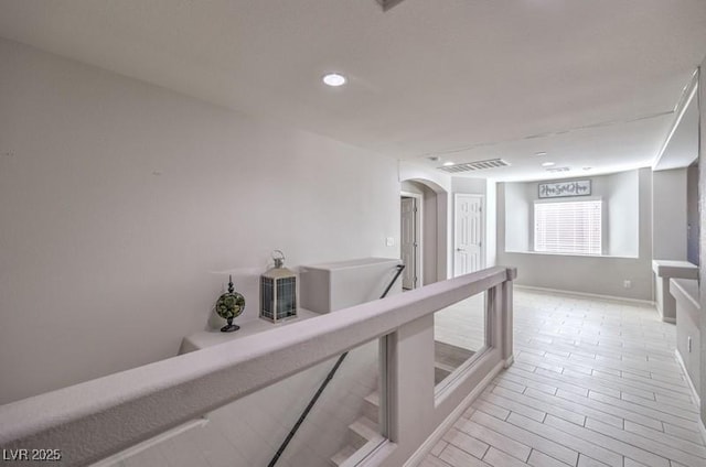 hall featuring arched walkways, light wood finished floors, recessed lighting, visible vents, and baseboards