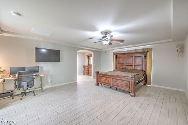 bedroom with baseboards, arched walkways, a raised ceiling, a ceiling fan, and light wood-type flooring