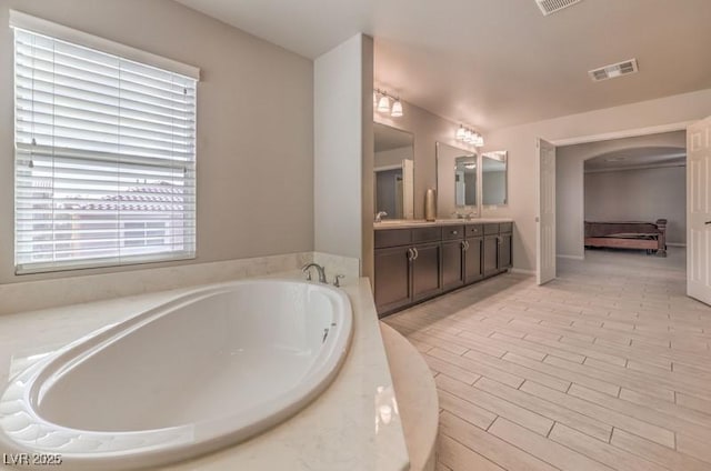 ensuite bathroom featuring double vanity, wood finished floors, a garden tub, and visible vents