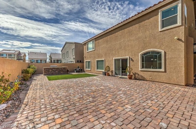 rear view of property featuring an outdoor fire pit, a patio area, a fenced backyard, and stucco siding