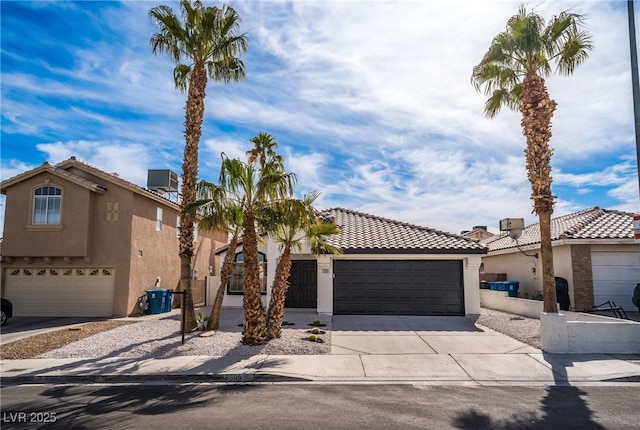 mediterranean / spanish-style home featuring a tiled roof, stucco siding, driveway, and central AC