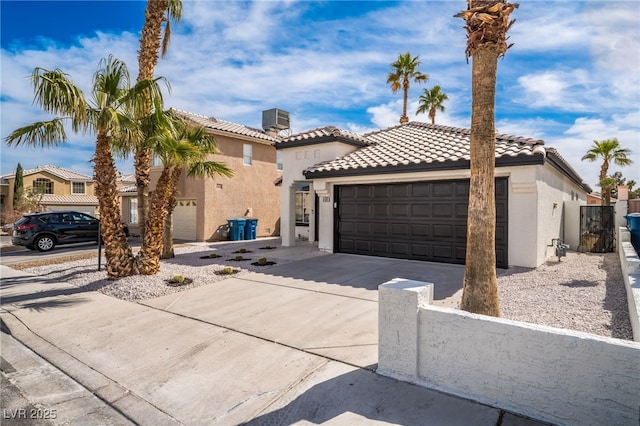 mediterranean / spanish home featuring stucco siding, a tiled roof, concrete driveway, and fence