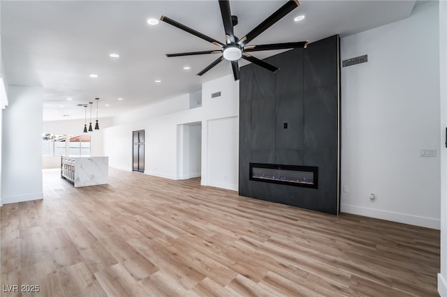 unfurnished living room with visible vents, light wood-style flooring, a fireplace, and ceiling fan