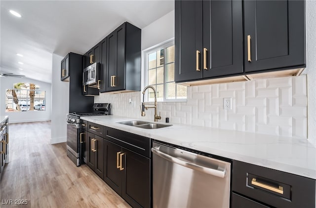 kitchen featuring dark cabinetry, a sink, decorative backsplash, stainless steel appliances, and light wood-style floors