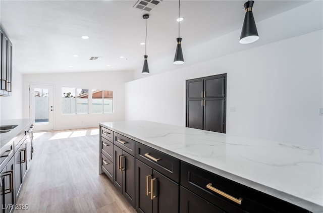 kitchen featuring light stone counters, visible vents, hanging light fixtures, and light wood finished floors