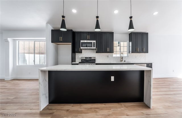 kitchen with light wood-type flooring, decorative backsplash, appliances with stainless steel finishes, a large island, and a sink