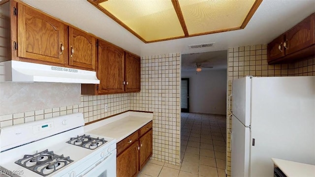 kitchen with white appliances, light tile patterned floors, visible vents, ceiling fan, and under cabinet range hood