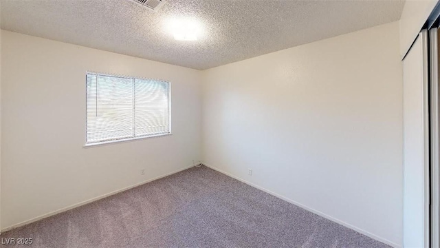 carpeted spare room featuring visible vents, a textured ceiling, and baseboards