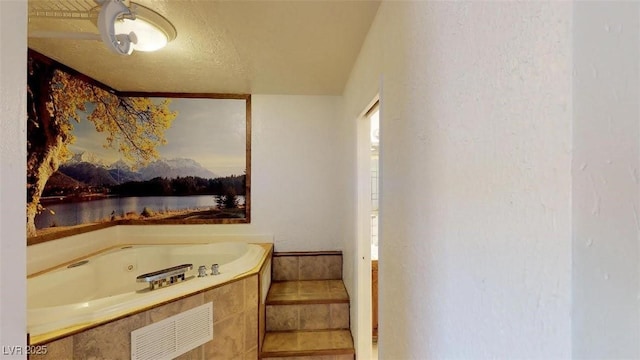 full bathroom featuring a tub with jets, a textured ceiling, visible vents, and a water view