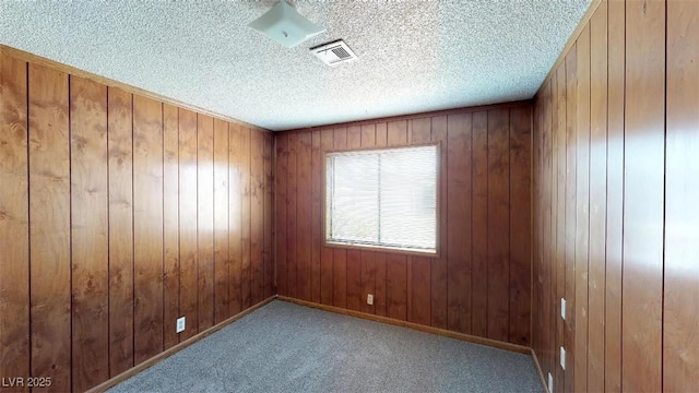 empty room featuring wooden walls, baseboards, visible vents, carpet floors, and a textured ceiling