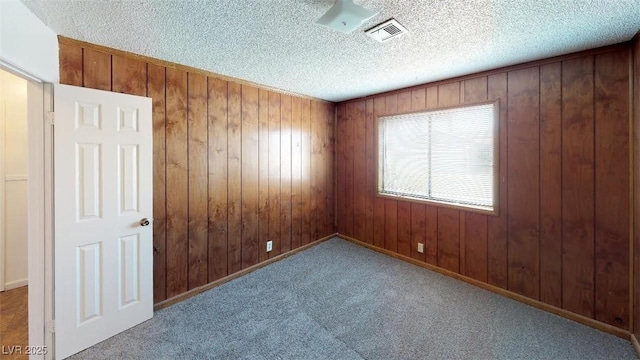 carpeted spare room with visible vents, wood walls, and a textured ceiling