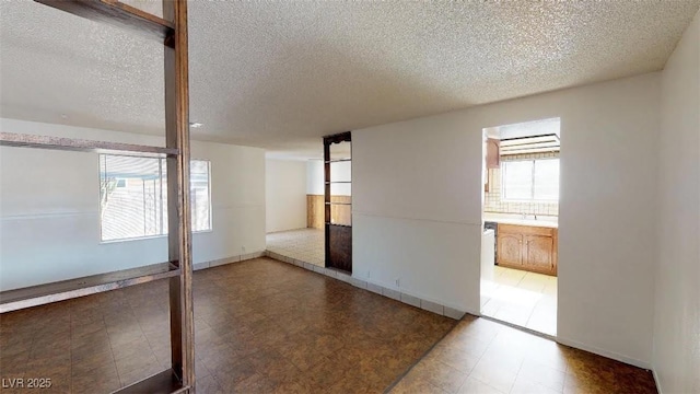 unfurnished room with light floors, a textured ceiling, and baseboards