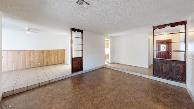 spare room featuring visible vents, a textured ceiling, wood walls, wainscoting, and ceiling fan