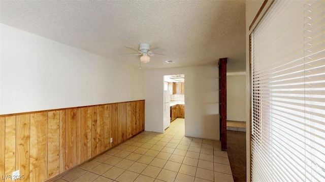 unfurnished room with a wainscoted wall, a ceiling fan, a textured ceiling, wooden walls, and light tile patterned floors