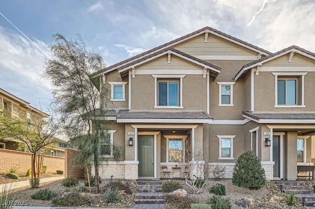 craftsman house with stone siding, a tile roof, fence, and stucco siding