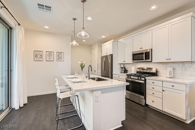 kitchen with dark wood-type flooring, a sink, visible vents, appliances with stainless steel finishes, and an island with sink