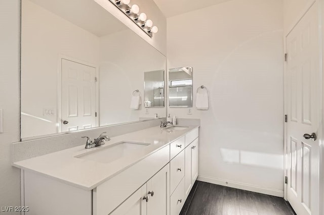 full bathroom with double vanity, baseboards, a sink, and wood finished floors