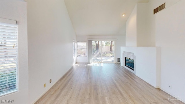 unfurnished living room featuring high vaulted ceiling, light wood finished floors, a tiled fireplace, and visible vents