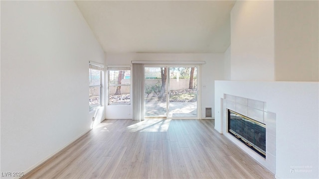 unfurnished living room featuring high vaulted ceiling, a tile fireplace, plenty of natural light, and light wood finished floors