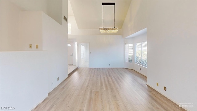 unfurnished living room with visible vents, light wood finished floors, and a high ceiling