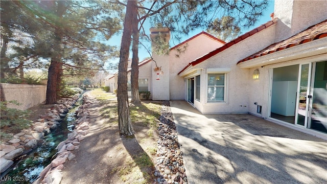 view of side of property featuring a chimney, fence, a patio, and stucco siding