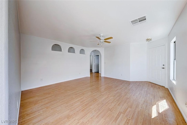 empty room with arched walkways, ceiling fan, light wood-style flooring, visible vents, and baseboards