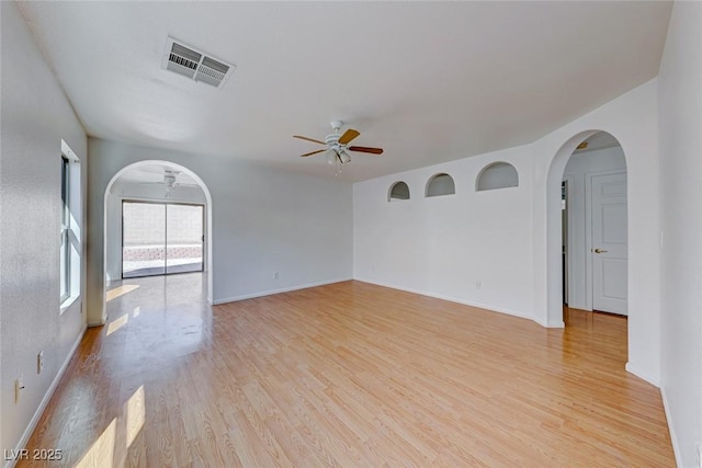 empty room with arched walkways, ceiling fan, light wood finished floors, and visible vents