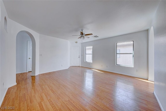 unfurnished room with arched walkways, a ceiling fan, baseboards, visible vents, and light wood-style floors