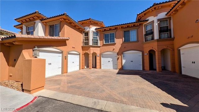 view of front of house with an attached garage, driveway, a tiled roof, and stucco siding