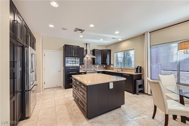 kitchen featuring visible vents, decorative backsplash, wall chimney exhaust hood, a kitchen island, and stainless steel appliances