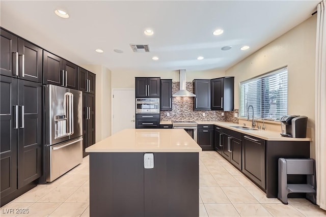 kitchen with a sink, visible vents, wall chimney range hood, appliances with stainless steel finishes, and a center island