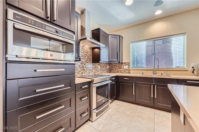 kitchen with a sink, light countertops, wall chimney range hood, appliances with stainless steel finishes, and decorative backsplash