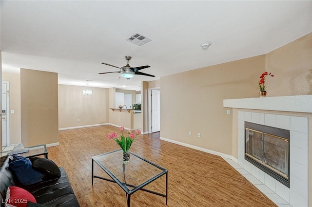 living area featuring visible vents, a tiled fireplace, ceiling fan, wood finished floors, and baseboards