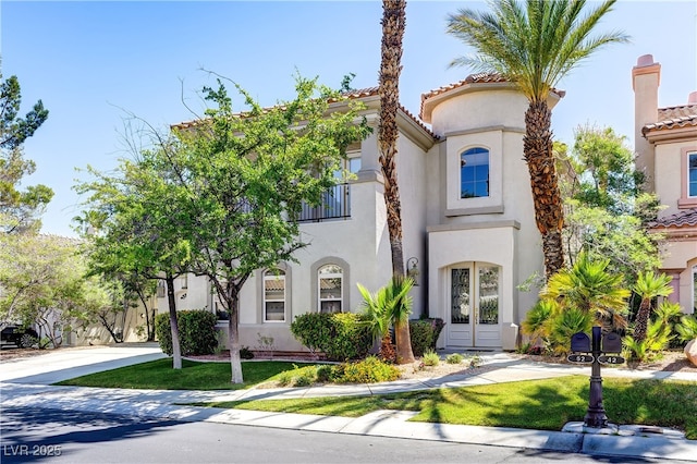 mediterranean / spanish-style house with concrete driveway, french doors, a tile roof, and stucco siding