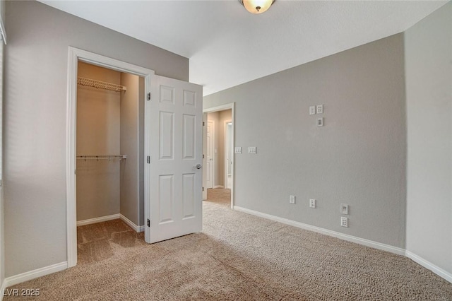 unfurnished bedroom featuring a walk in closet, a closet, light colored carpet, and baseboards