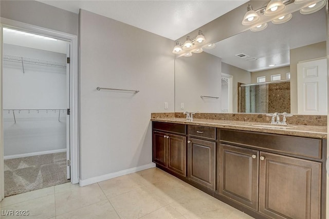 bathroom with double vanity, a stall shower, baseboards, a walk in closet, and a sink