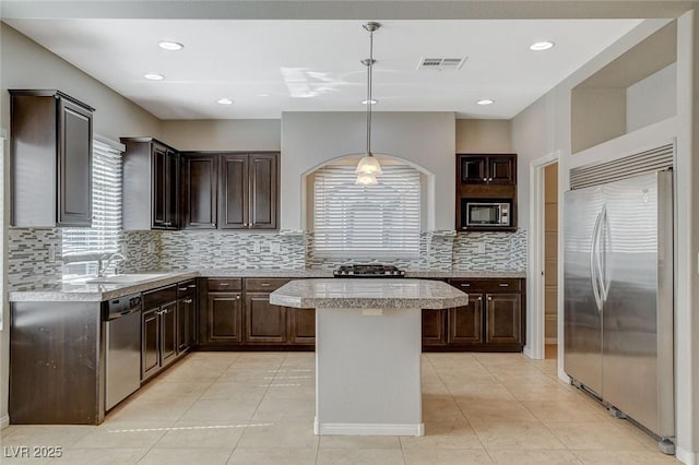 kitchen featuring dark brown cabinetry, light countertops, a sink, and built in appliances