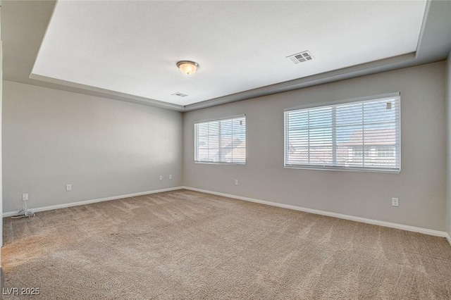 carpeted spare room featuring baseboards, visible vents, and a tray ceiling