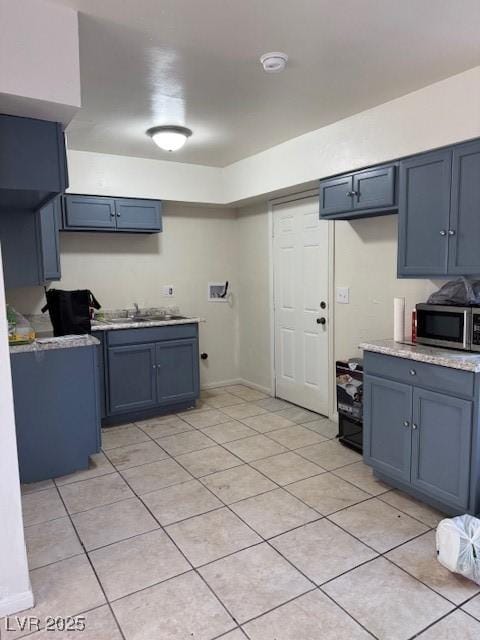 kitchen with blue cabinets, light countertops, stainless steel microwave, and a sink