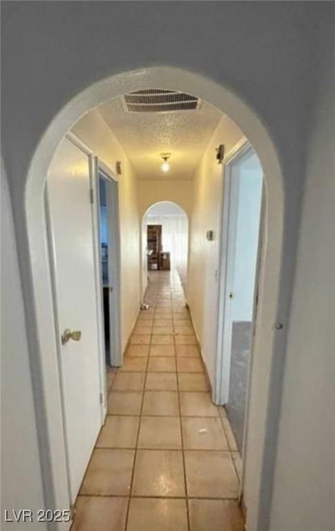 hallway featuring a textured ceiling, light tile patterned flooring, arched walkways, and visible vents