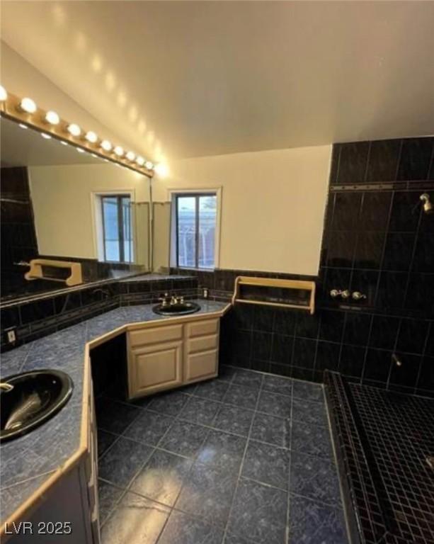 bathroom featuring a wainscoted wall, tile patterned floors, vaulted ceiling, vanity, and tile walls