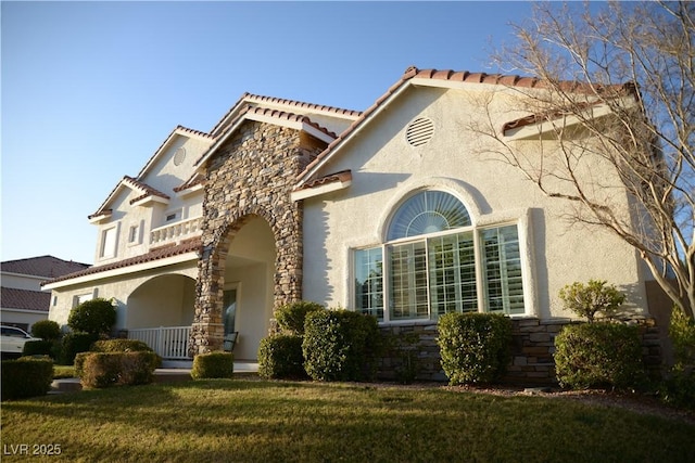 mediterranean / spanish home featuring a front lawn, a porch, stone siding, and stucco siding