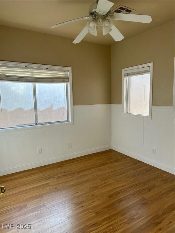 unfurnished room featuring a wainscoted wall, wood finished floors, visible vents, and a ceiling fan