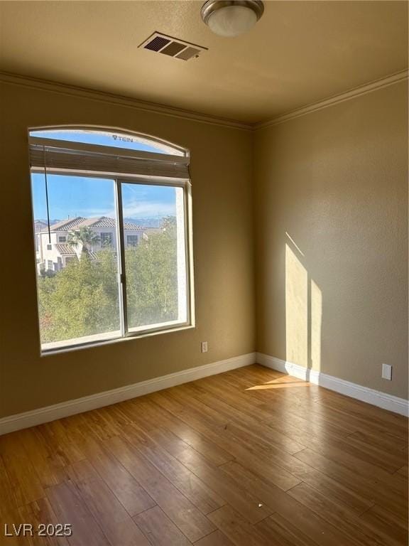 unfurnished room with visible vents, crown molding, baseboards, and wood finished floors