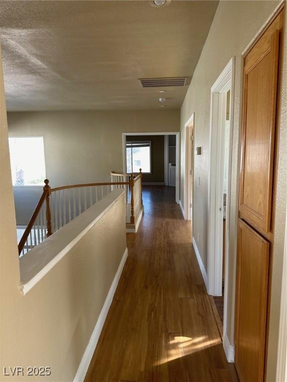 hallway featuring baseboards, visible vents, dark wood-type flooring, and an upstairs landing